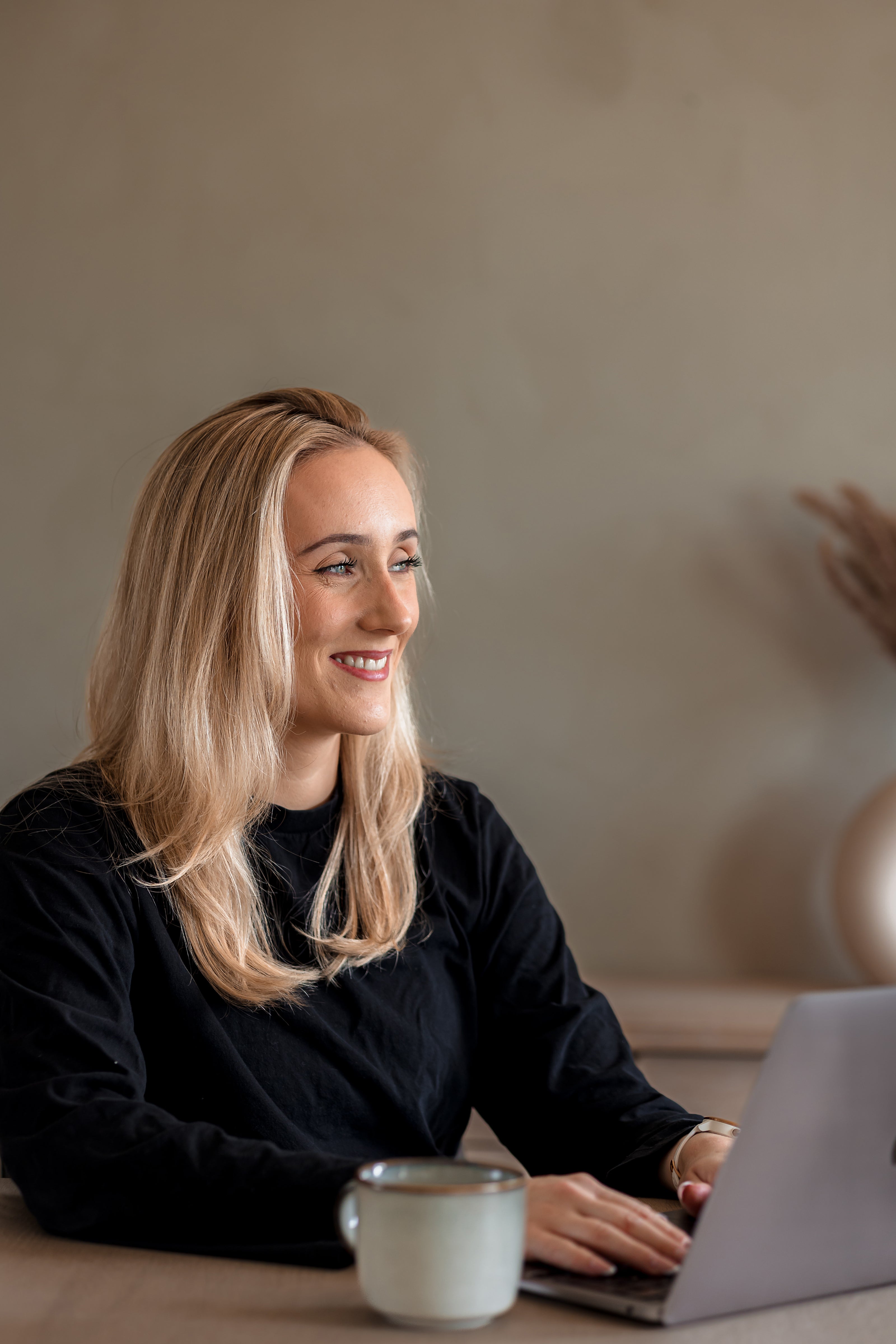 Elena Mellingen smiler mens hun sitter ved kjøkkenbordet med en bærbar PC foran seg.